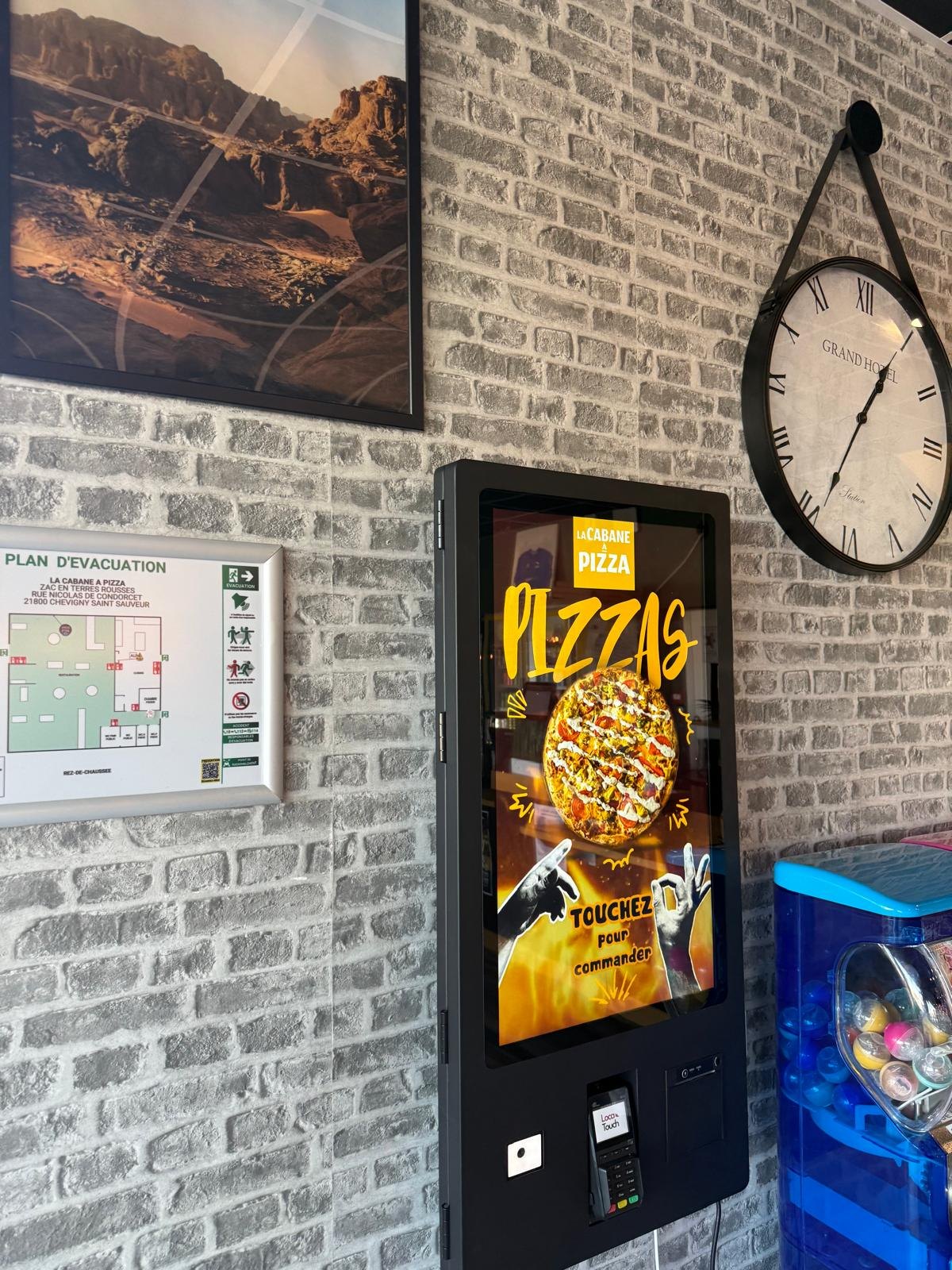 Borne de commande murale de pizzeria près d'une horloge, mur de briques